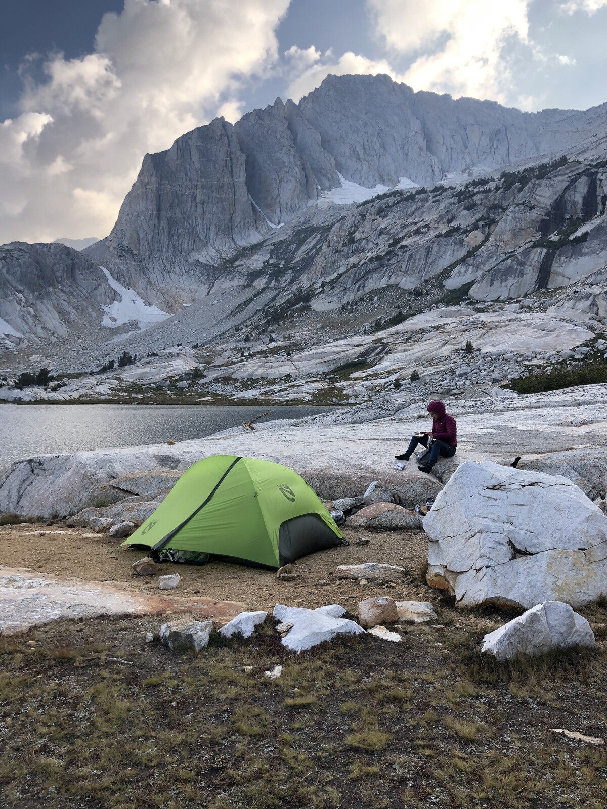 Green tent camping at alpine lake with dramatic peak backdrop