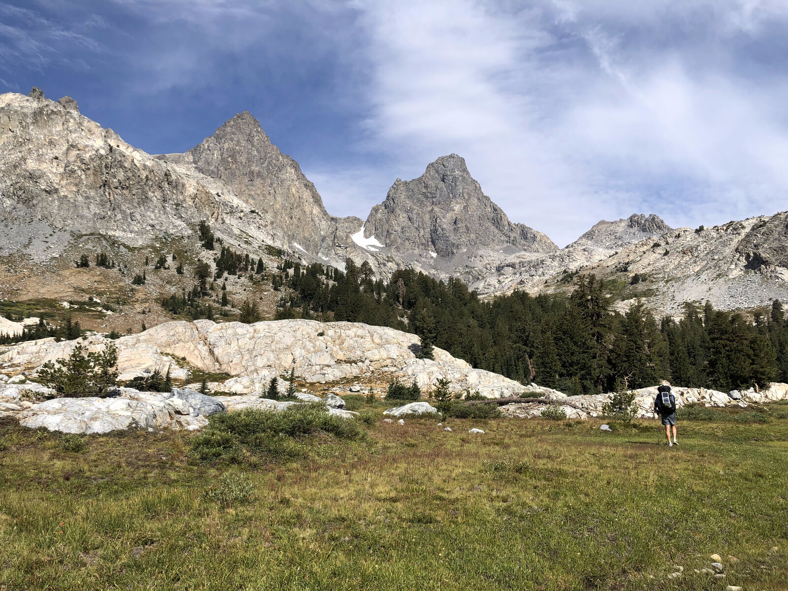 Hiker in alpine meadow with extensive peak views