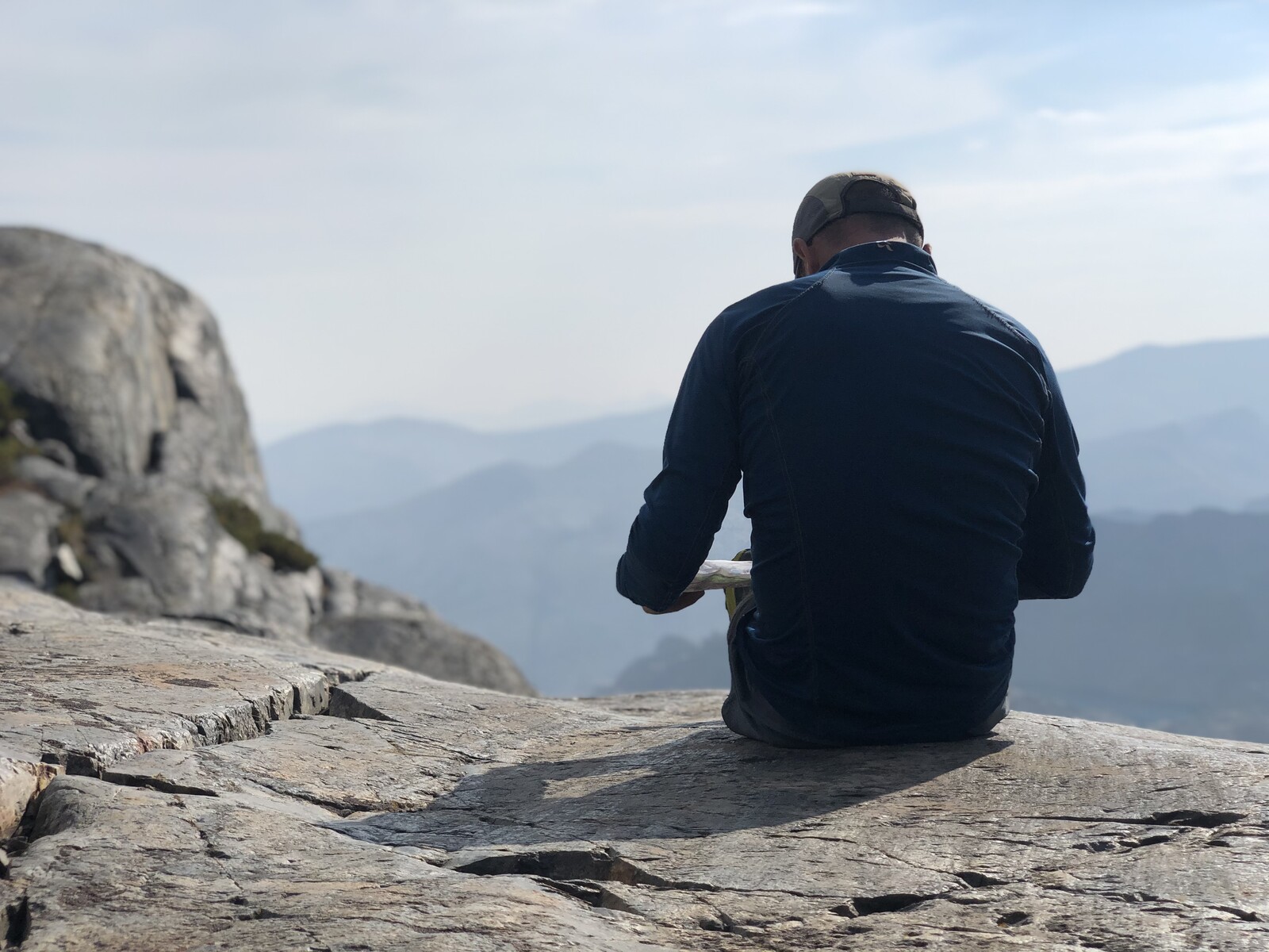 Hiker sitting on rock overlooking vast mountain landscape